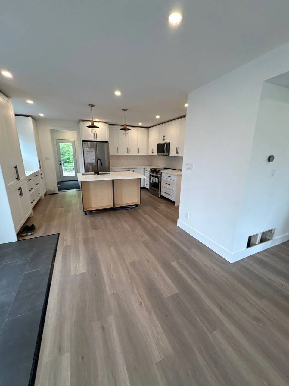 Modern kitchen with white cabinets, stainless steel appliances, an island with a black sink, pendant lighting, and wood flooring.