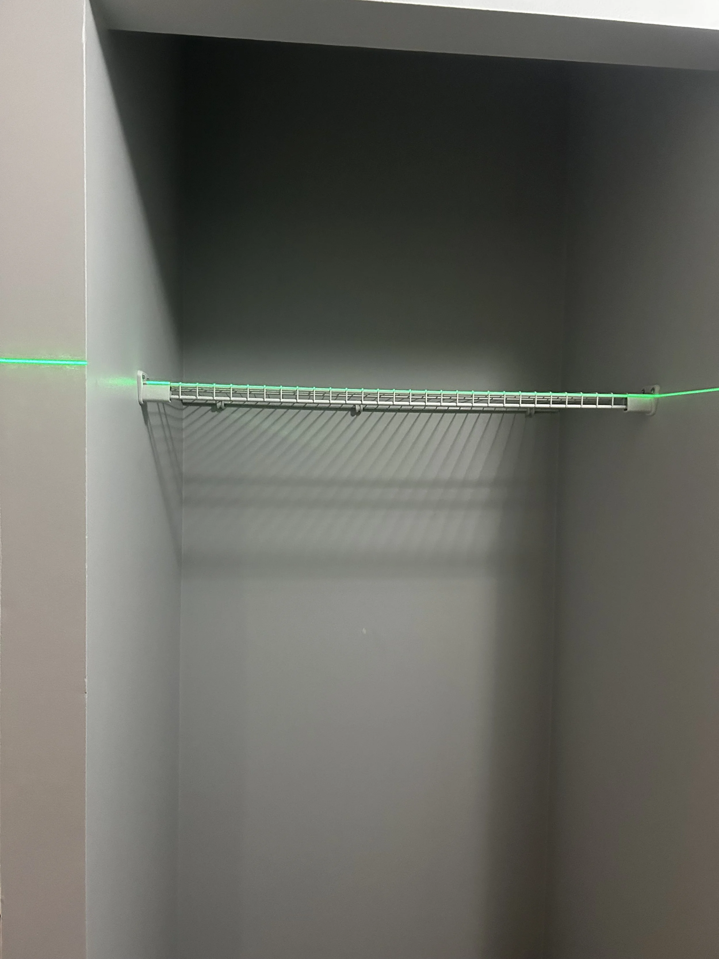 Empty gray closet with a wire shelf and green LED lighting strip at the back.