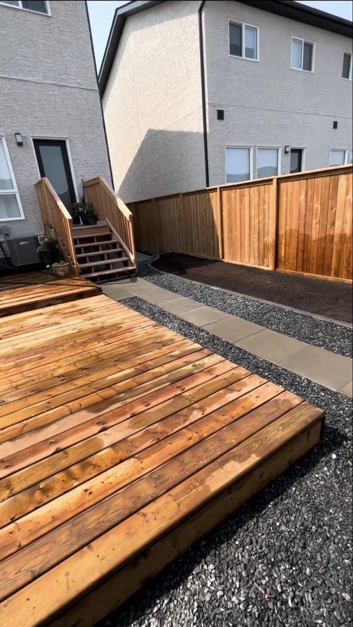 Backyard with wooden deck, pathway, and a wooden fence, neighboring houses visible in the background.