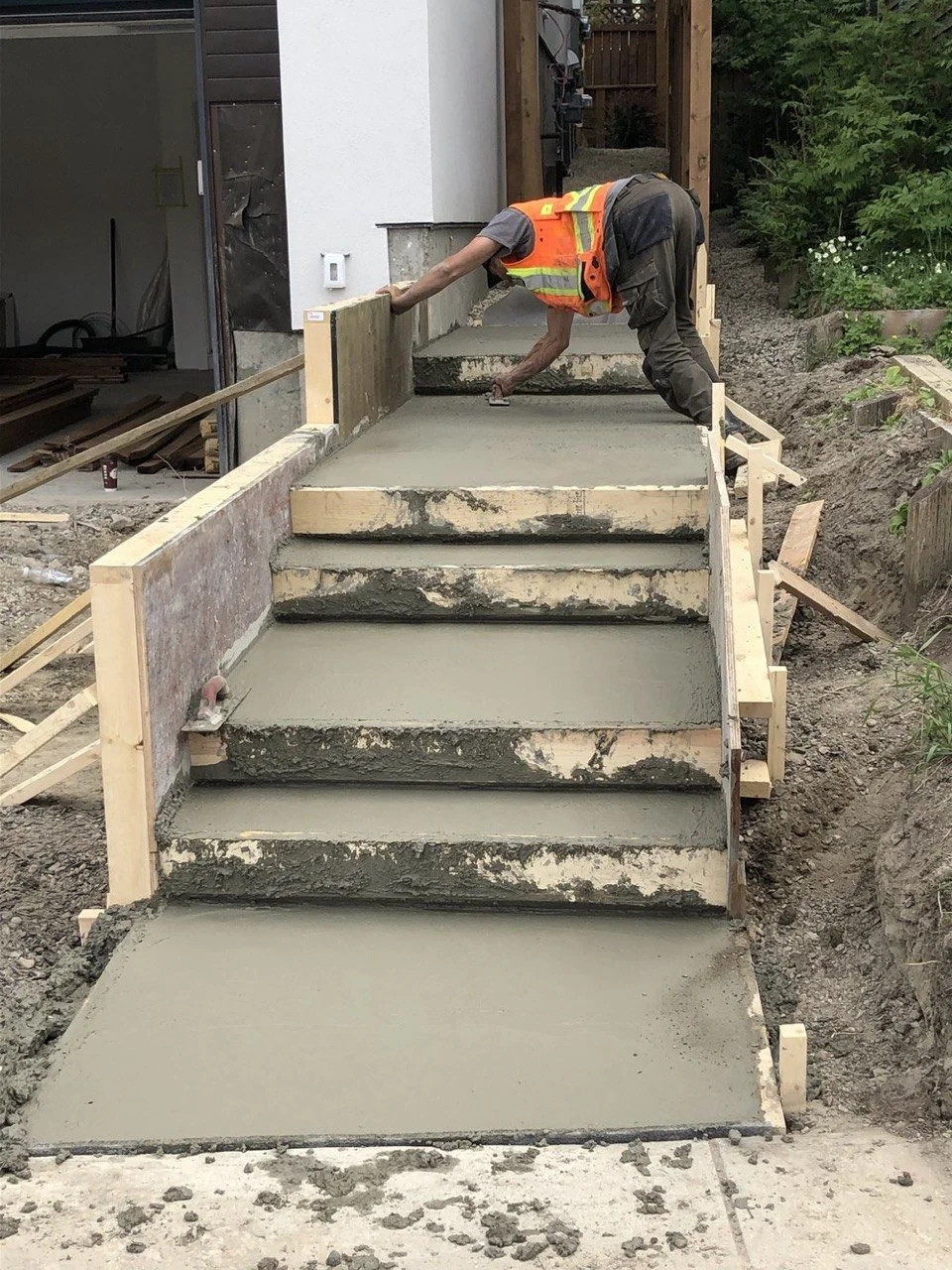 Construction worker smoothing wet concrete on stairs at a residential building site.