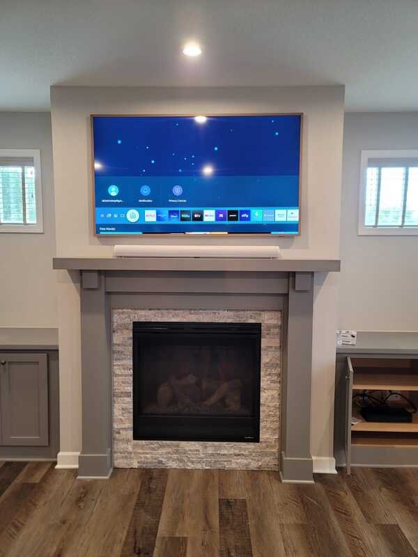 Living room fireplace with a mounted flat-screen TV above it, decorated in a modern style with gray trim and stone facing around the fireplace, flanked by small built-in cabinets, and a window on each side.