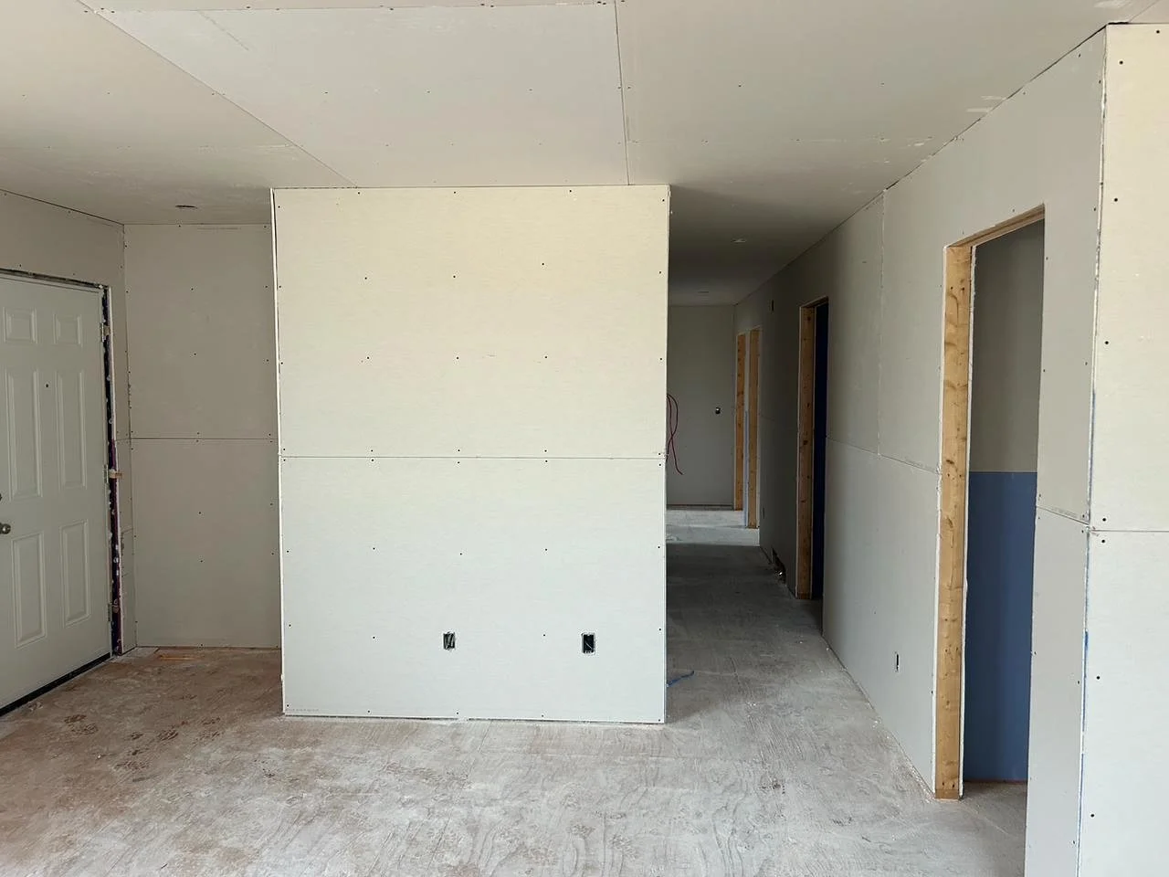 Interior of a house under construction with white drywall partially installed, door frames without doors, and exposed floor and ceiling.