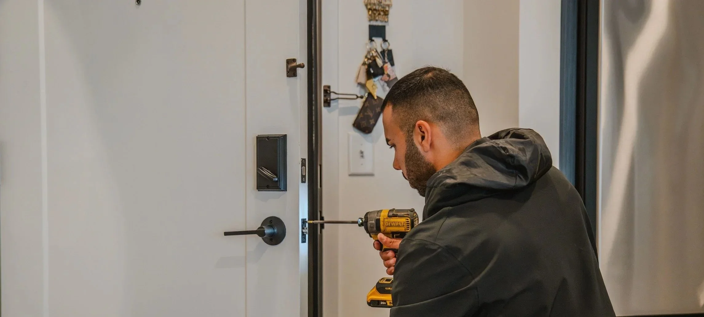 Man using a yellow and black DeWalt cordless drill to install or repair a door lock on a white door in a modern home or apartment.