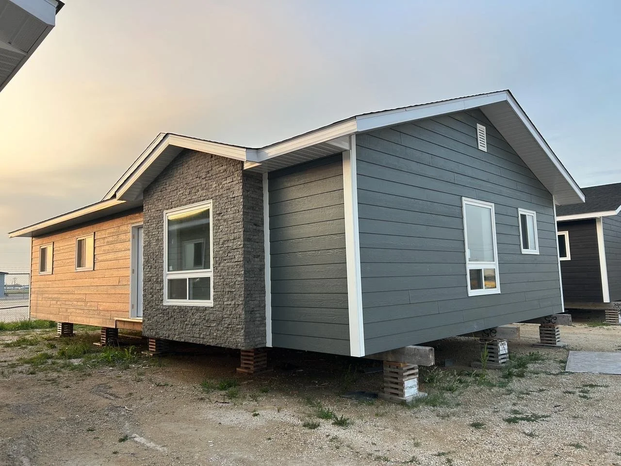 Unfinished house on concrete blocks with a combination of siding and brick exterior, situated in an open yard with patches of grass.