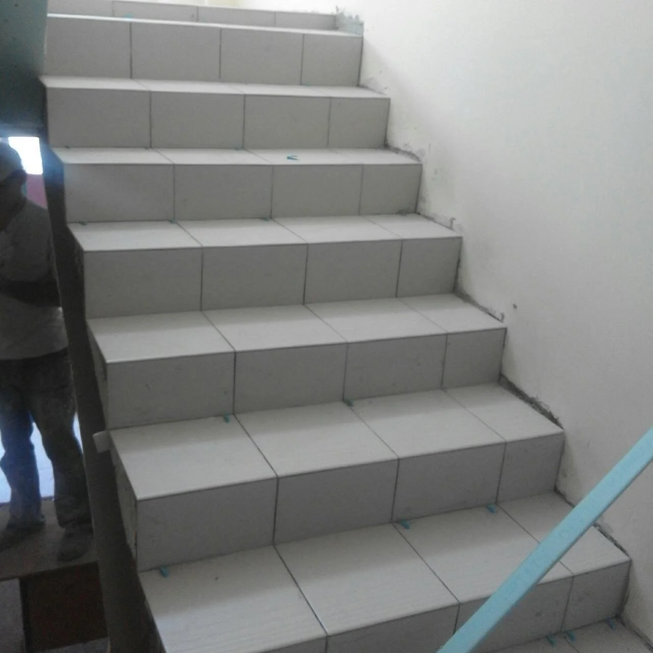 The image shows a staircase with white floor tiles and gray wall tiles, with some construction or renovation work in progress.