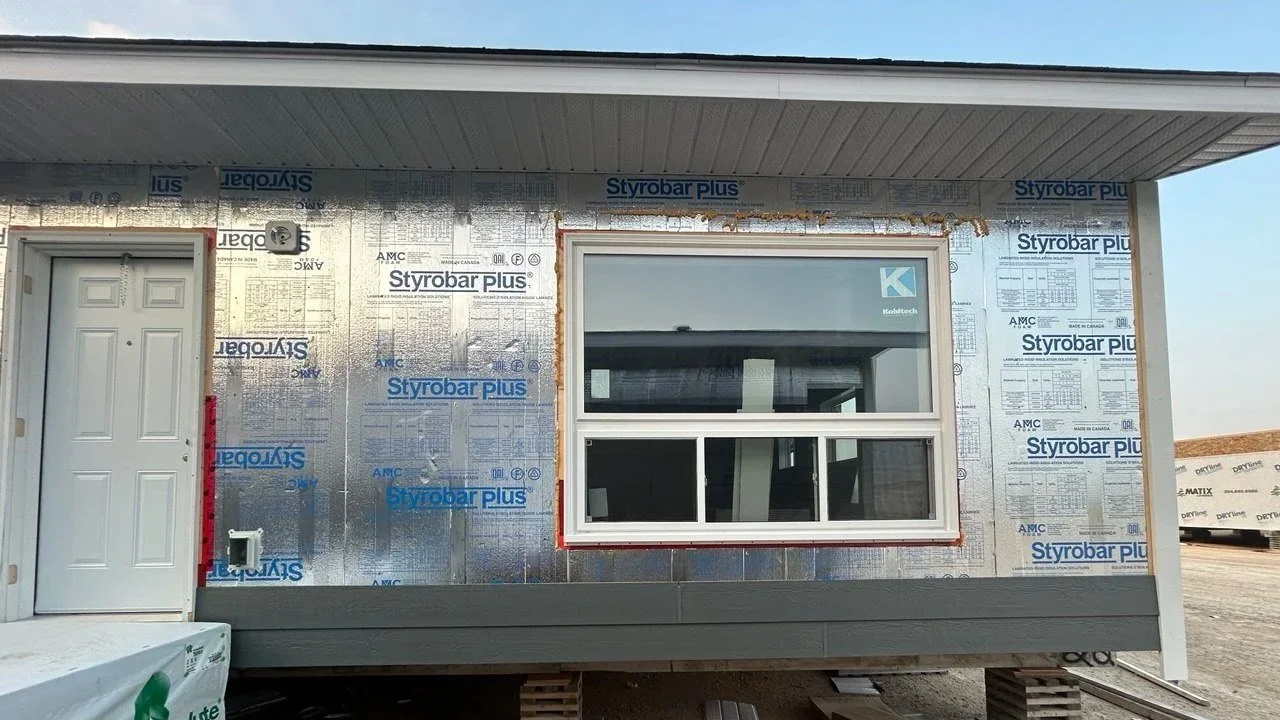 Exterior view of a house under construction, featuring a window, a door, and wall insulation with Styrobar Plus panels.