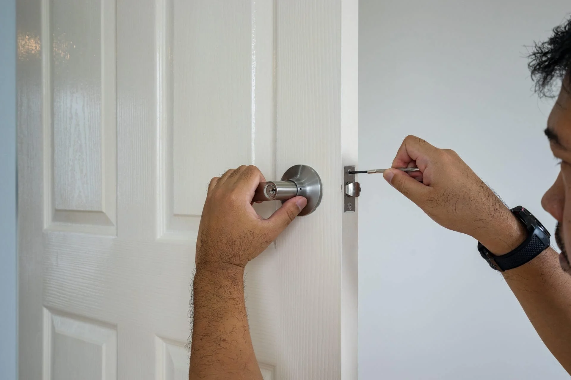 Person installing a doorknob on a white interior door using a screwdriver.