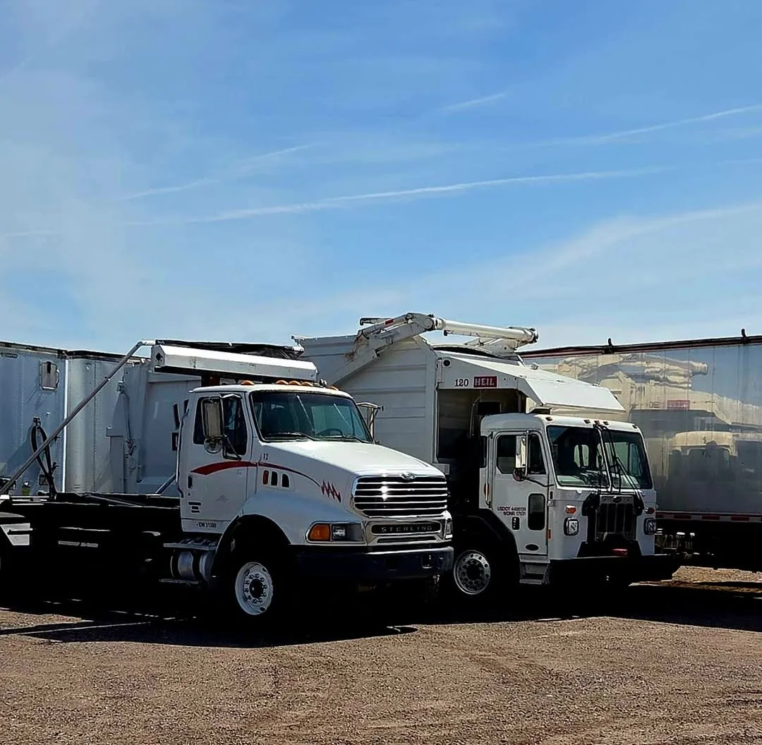 Two white fire trucks with equipment, parked on a gravel lot under a blue sky.