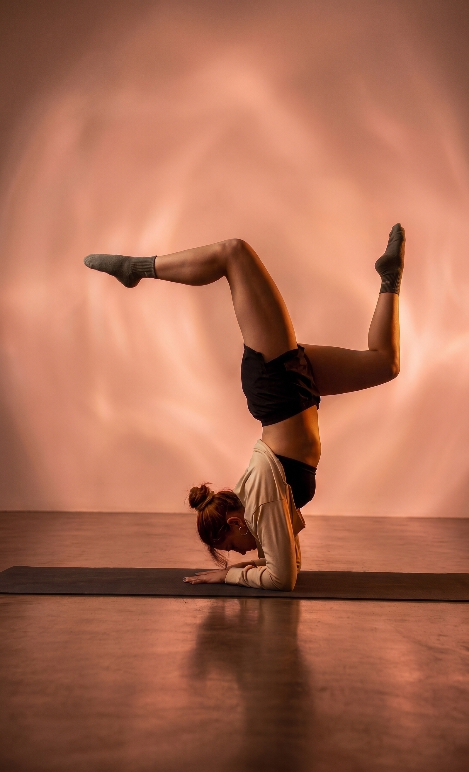Una persona haciendo una posición de yoga en la que está en cuclillas con las piernas en forma de V y el cuerpo en forma de arco invertido, en un estudio con iluminación suave.