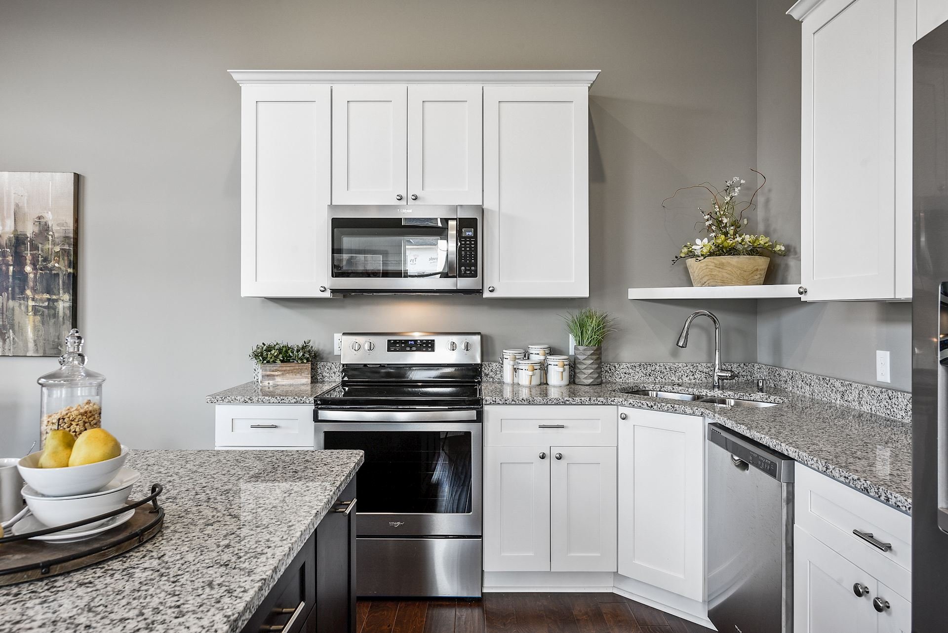 Modern kitchen with white cabinets, stainless steel microwave and stove, granite countertops, a sink, potted plants, and decorative items.
