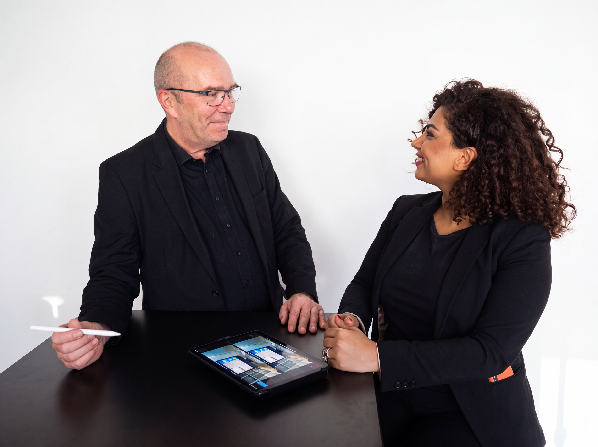 Der Optiker Ralf Überschär und eine Kundin des Zentriersystems OptikamPad schauen sich an und lächeln fröhlich. Vor ihnen liegt ein iPad mit der Software OptikamPad