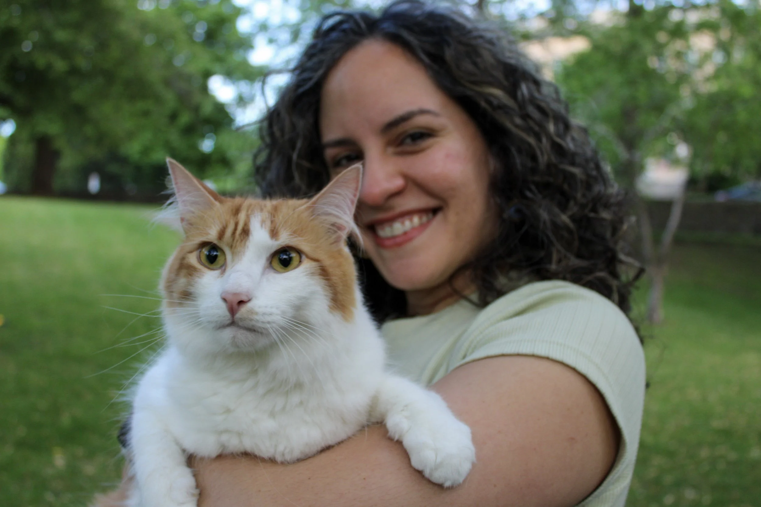 A woman pet sitter smiling and holding an orange and white cat outdoors.