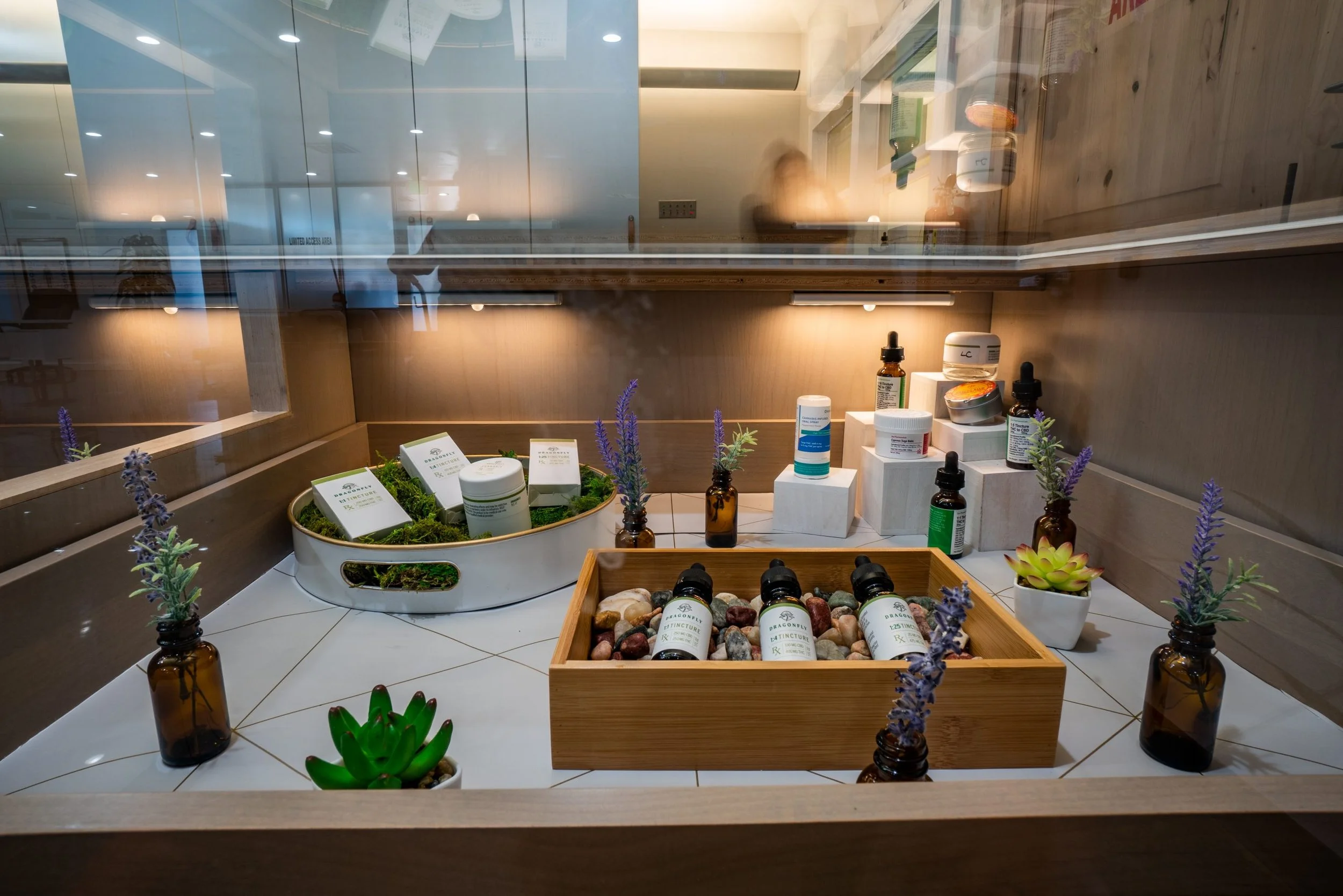 Display of herbal and natural wellness products, including essential oils, creams, and spritzers, arranged on a wooden and white surfaces surrounded by lavender plants and succulents.