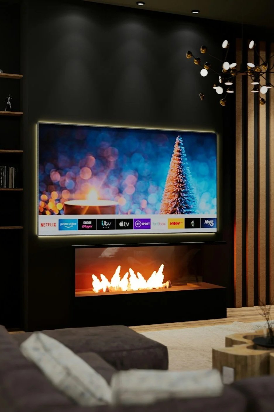 Living room with a wall-mounted TV displaying a festive holiday scene with a decorated Christmas tree and colorful lights, a modern electric fireplace below the TV with flames, a sofa with pillows in the foreground, and a decorative chandelier with multiple bulbs hanging from the ceiling.