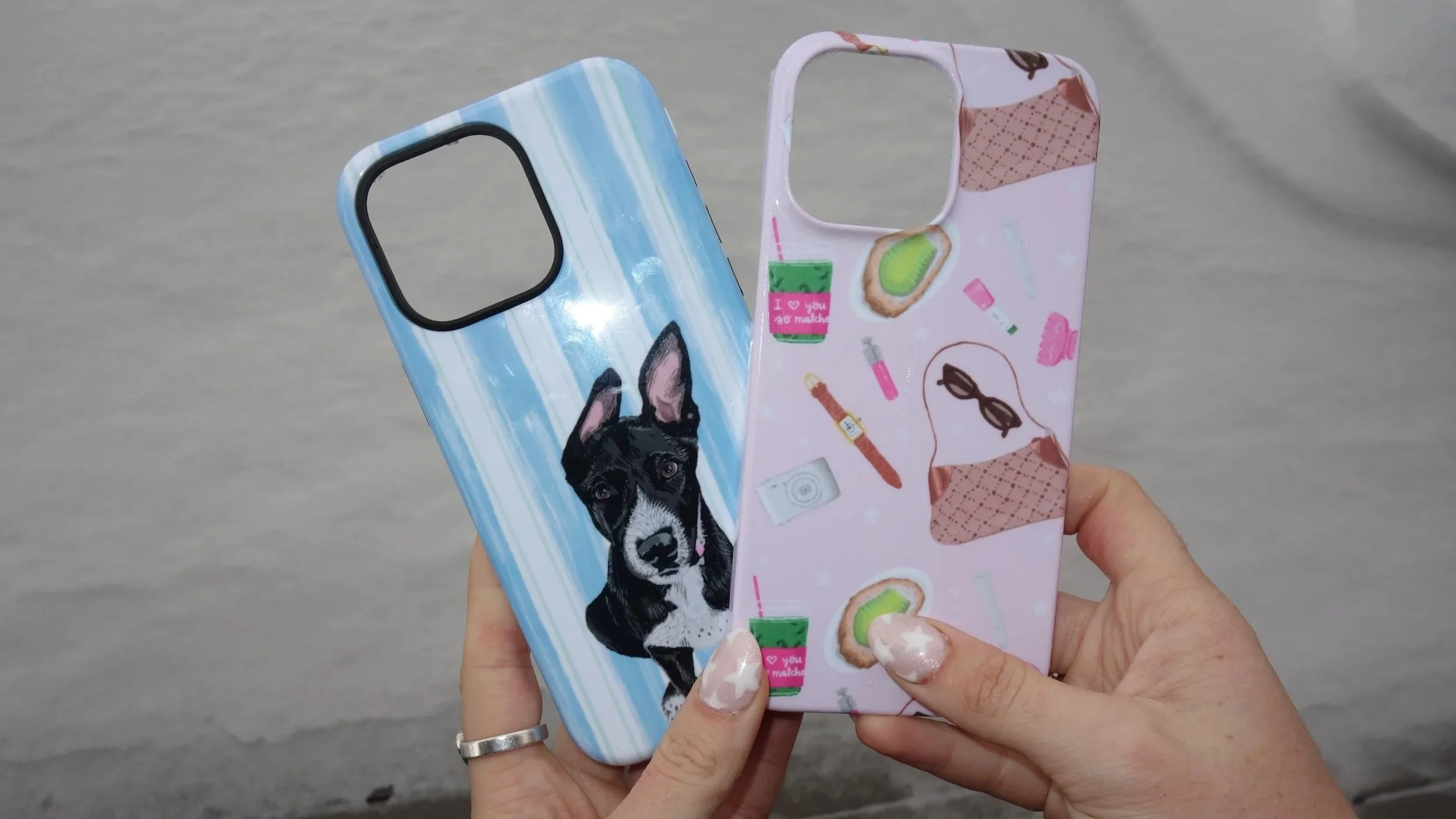 Two colorful phone cases being held up, one with a dog illustration and the other with a pattern of makeup and skincare items on a pink background.