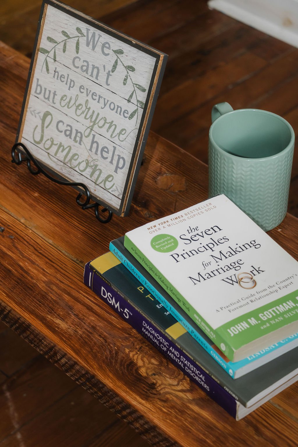 "we can't help someone but everyone can help someone" sign, coffee mug, stack of therapy-related books