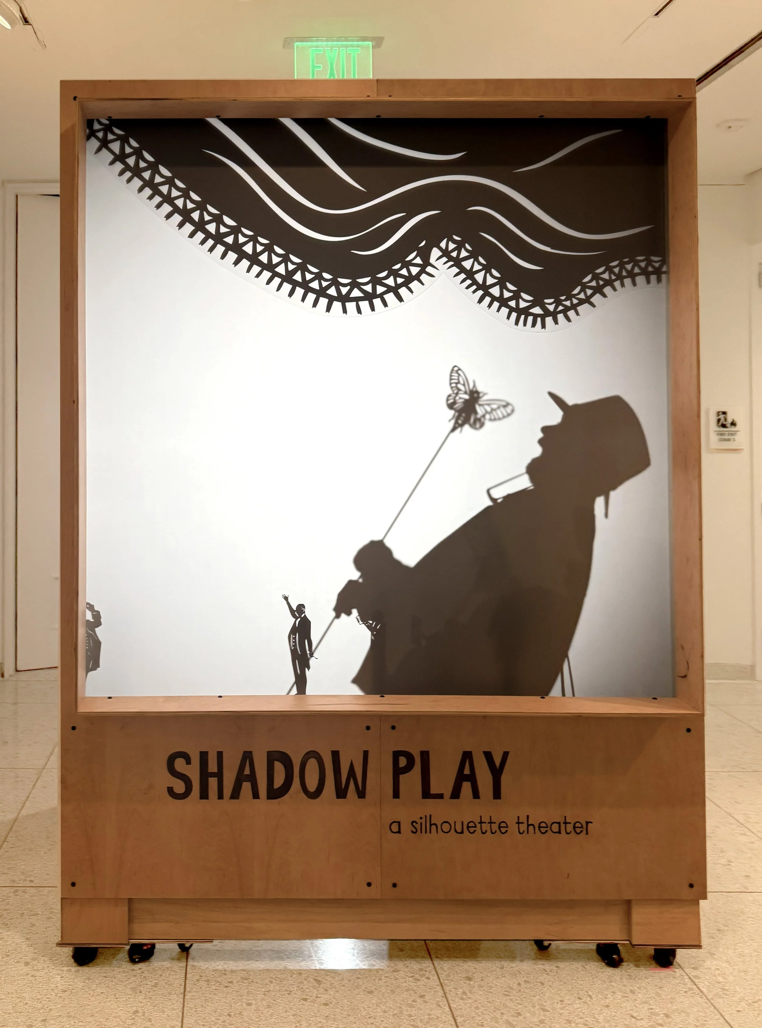 Museum display with black shadow silhouette artwork that depicts a person enjoying a custom-made museum display for Maryland Center for History and Culture, 'Shadow Play' and 'a silhouette theater' at the bottom.