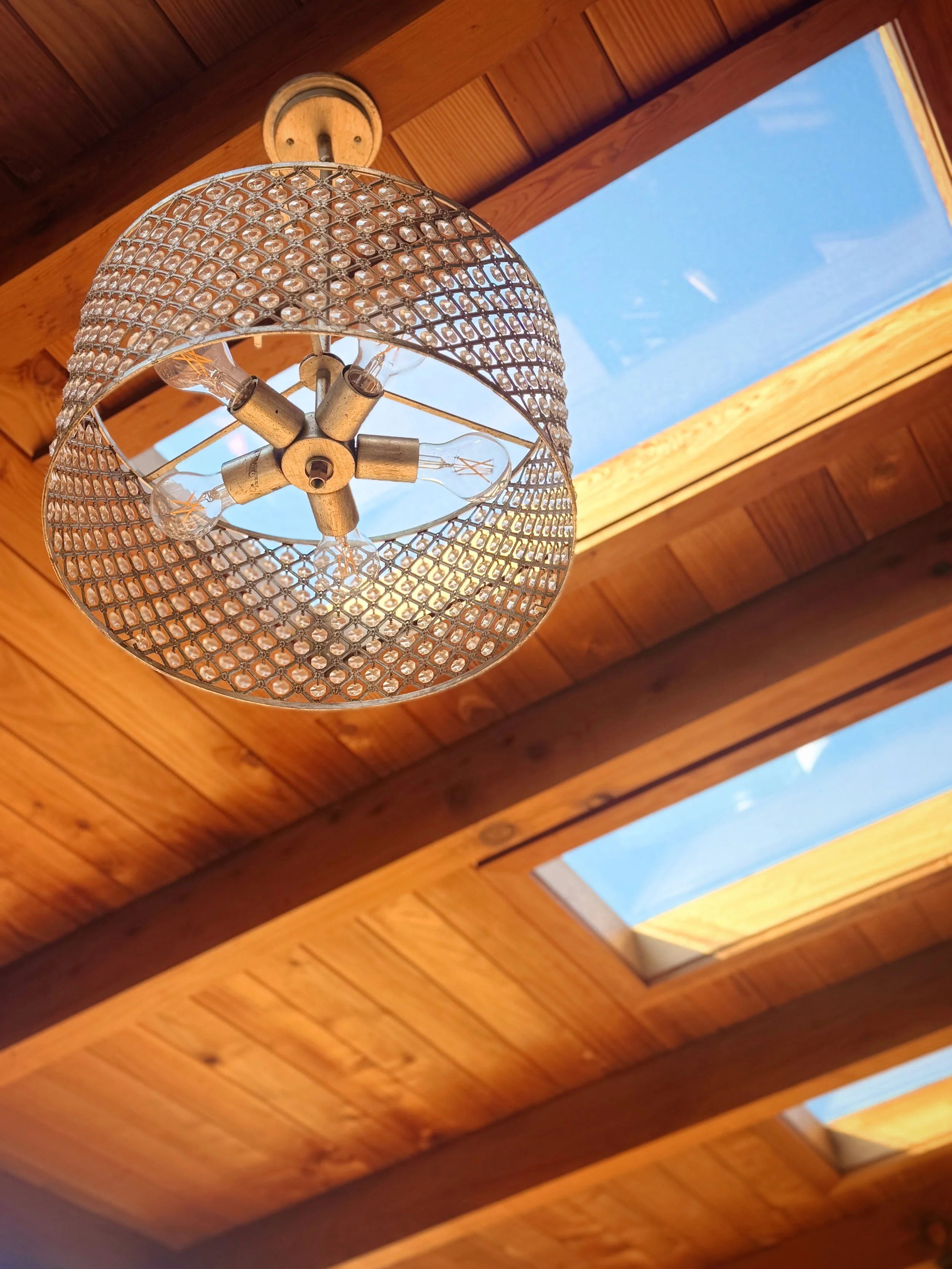 Wooden ceiling with three skylights and a chandelier fixture.