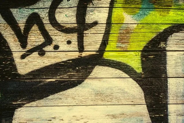 Close-up of graffiti art on wooden surface with black, yellow, and green colors.