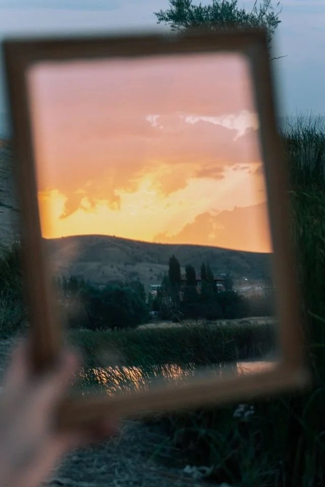hand holding a mirror that's capturing the sunset