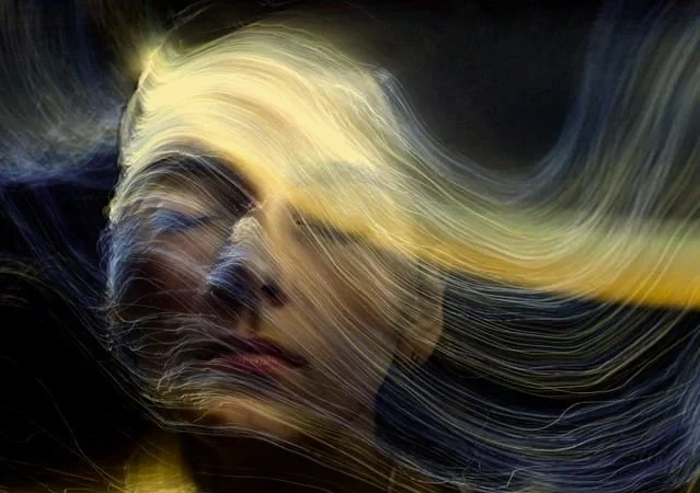 Close-up of a woman's face with flowing blonde hair, artistically portrayed with swirling light patterns.