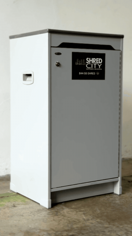 Metal trash bin labeled 'Shred City' positioned outdoors on a concrete surface