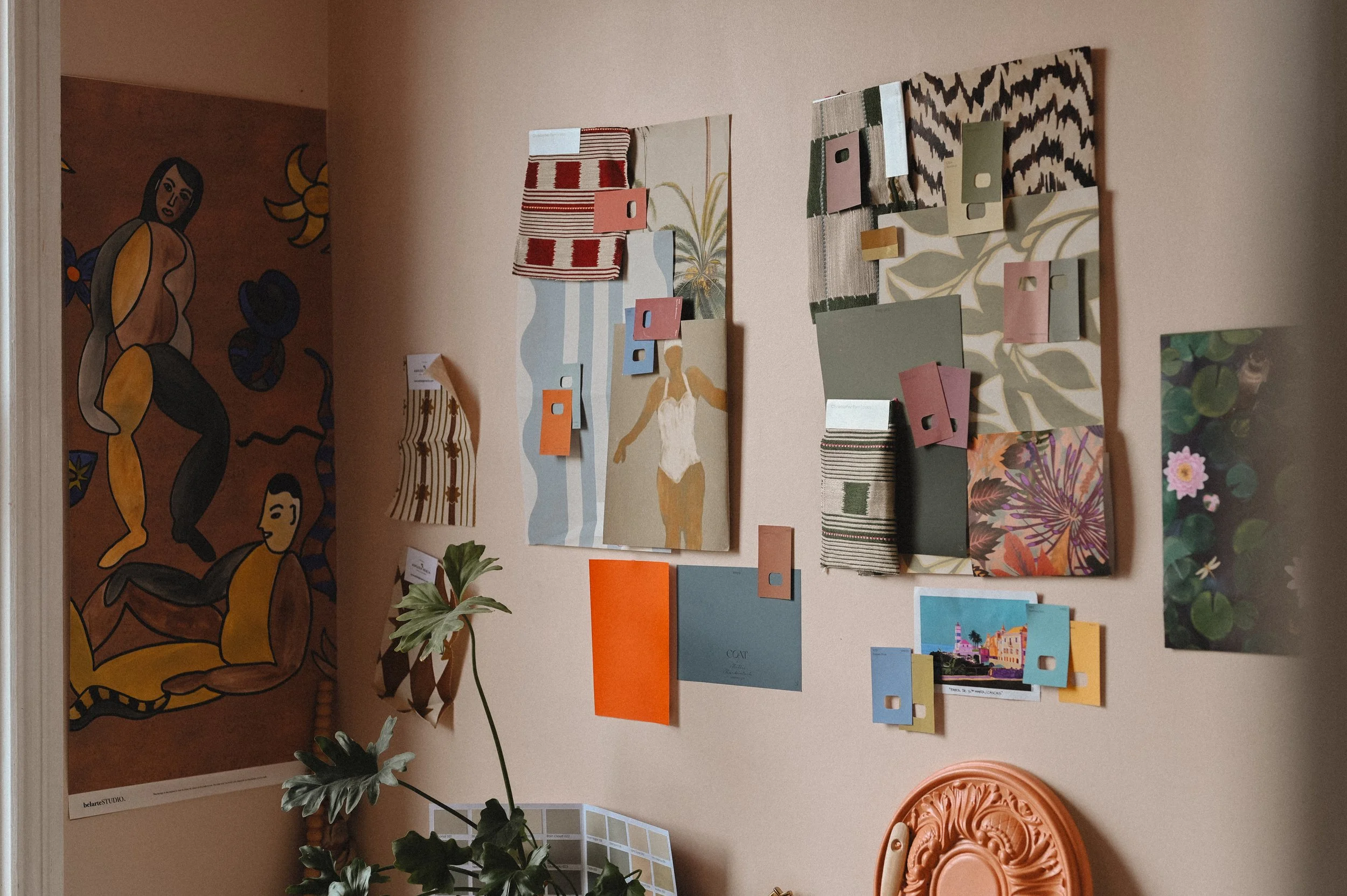 Wall decorated with color palette samples, artwork, and fabric swatches, with a mural featuring abstract human figures and floral patterns in the background.