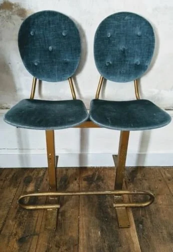 Two vintage blue upholstered chairs with gold metal legs placed against a white wall.