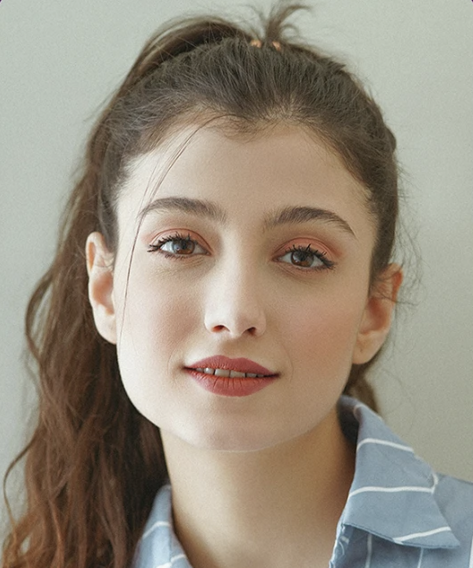 Close-up of a young woman with brown hair in a ponytail, wearing a blue striped shirt, looking at the camera with a slight smile.