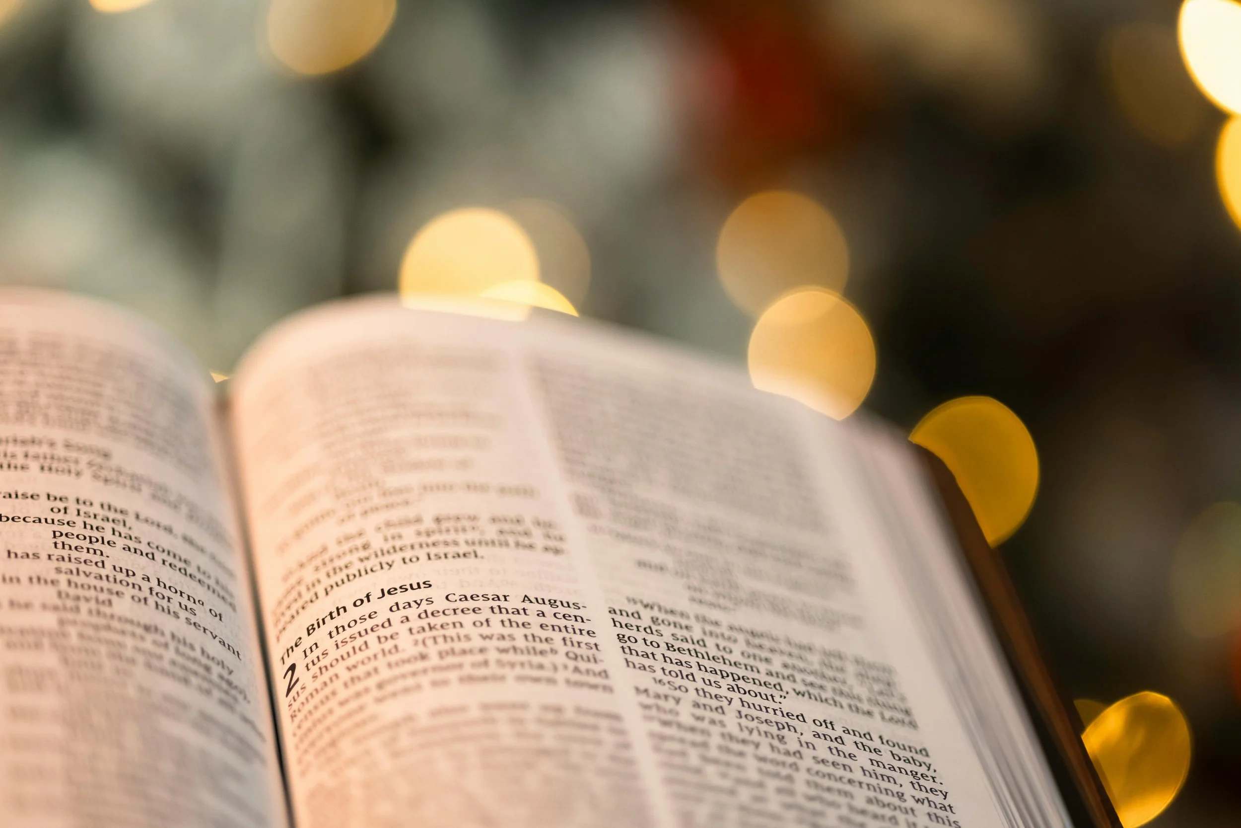 Open Bible with pages turned, in front of a blurred background of warm, circular bokeh lights.