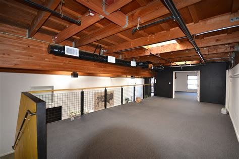 Empty indoor space with wooden ceiling, black railing, gray carpet, and a dark accent wall with a window.