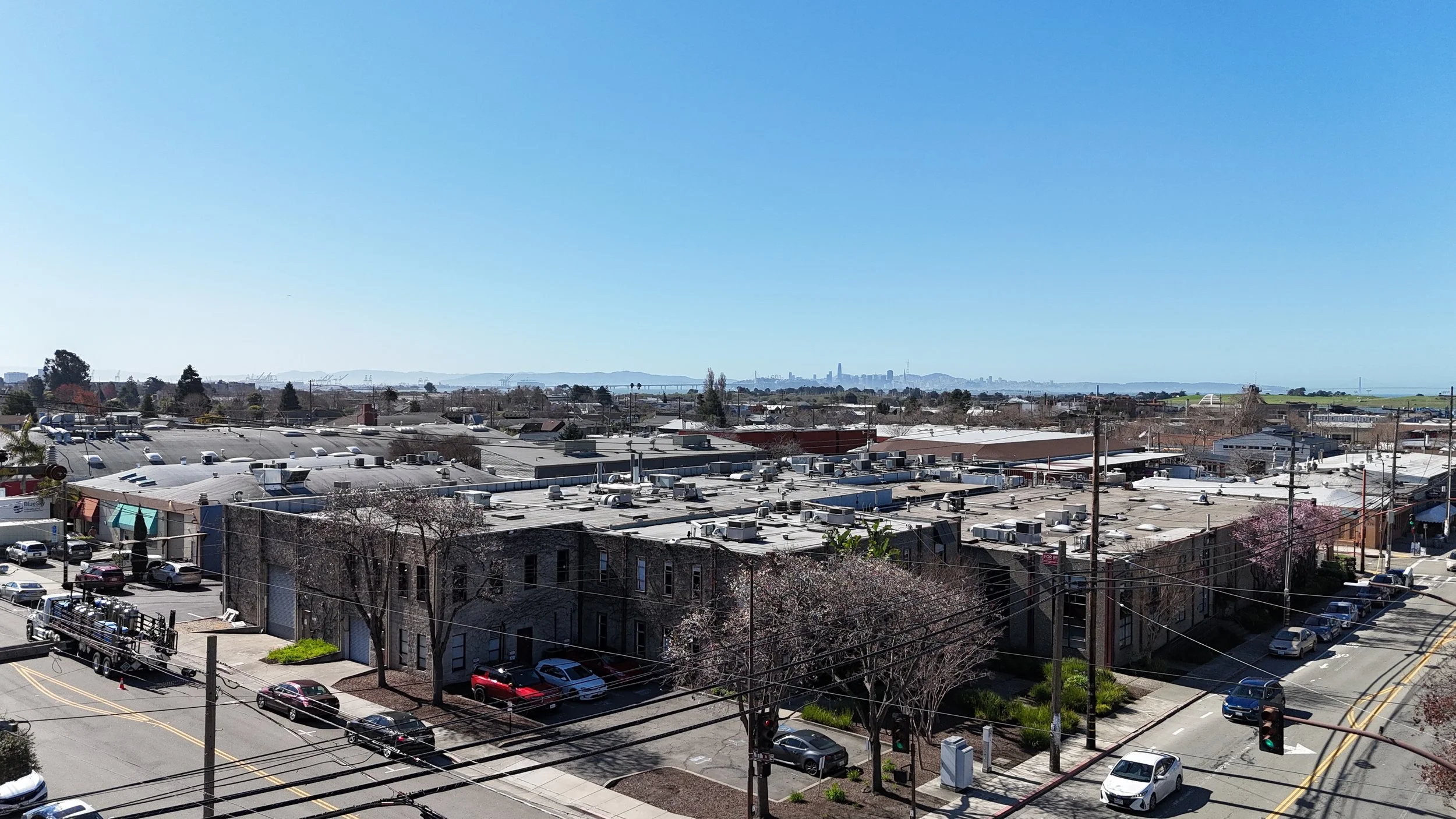 Cityscape view of rooftops, commercial buildings, and distant skyline with tall buildings under a clear blue sky.