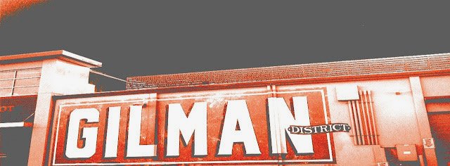 Close-up of a building with a sign that reads "GILMAN DISTRICT" in large, bold letters.