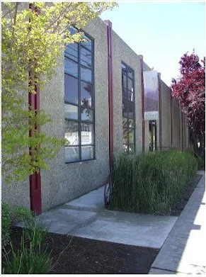 Exterior view of a modern building with large windows, surrounded by trees and greenery.