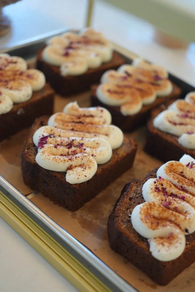 Chocolate brownies topped with cream, cinnamon, and dried flower petals on a tray.