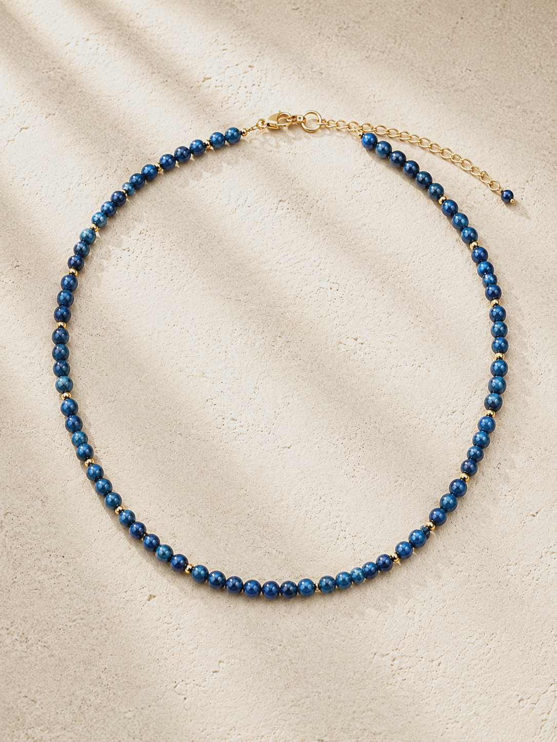 Blue beaded necklace with gold accents on a beige textured surface.