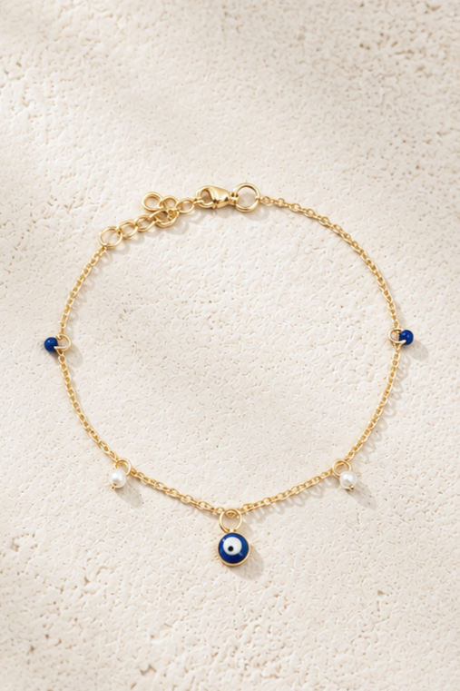 Gold bracelet with blue and white pearl-like charms, and a central evil eye charm.