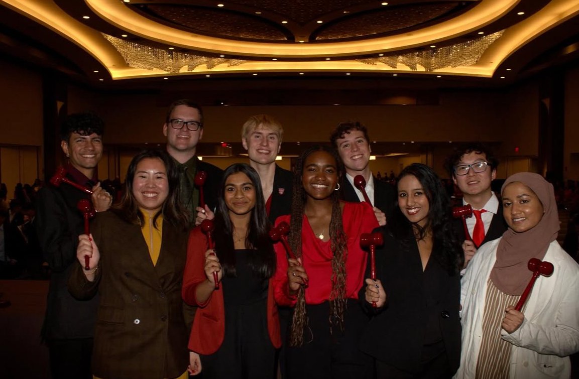 Group of ten young adults smiling and holding red gavel-shaped awards in a large, well-lit banquet hall.