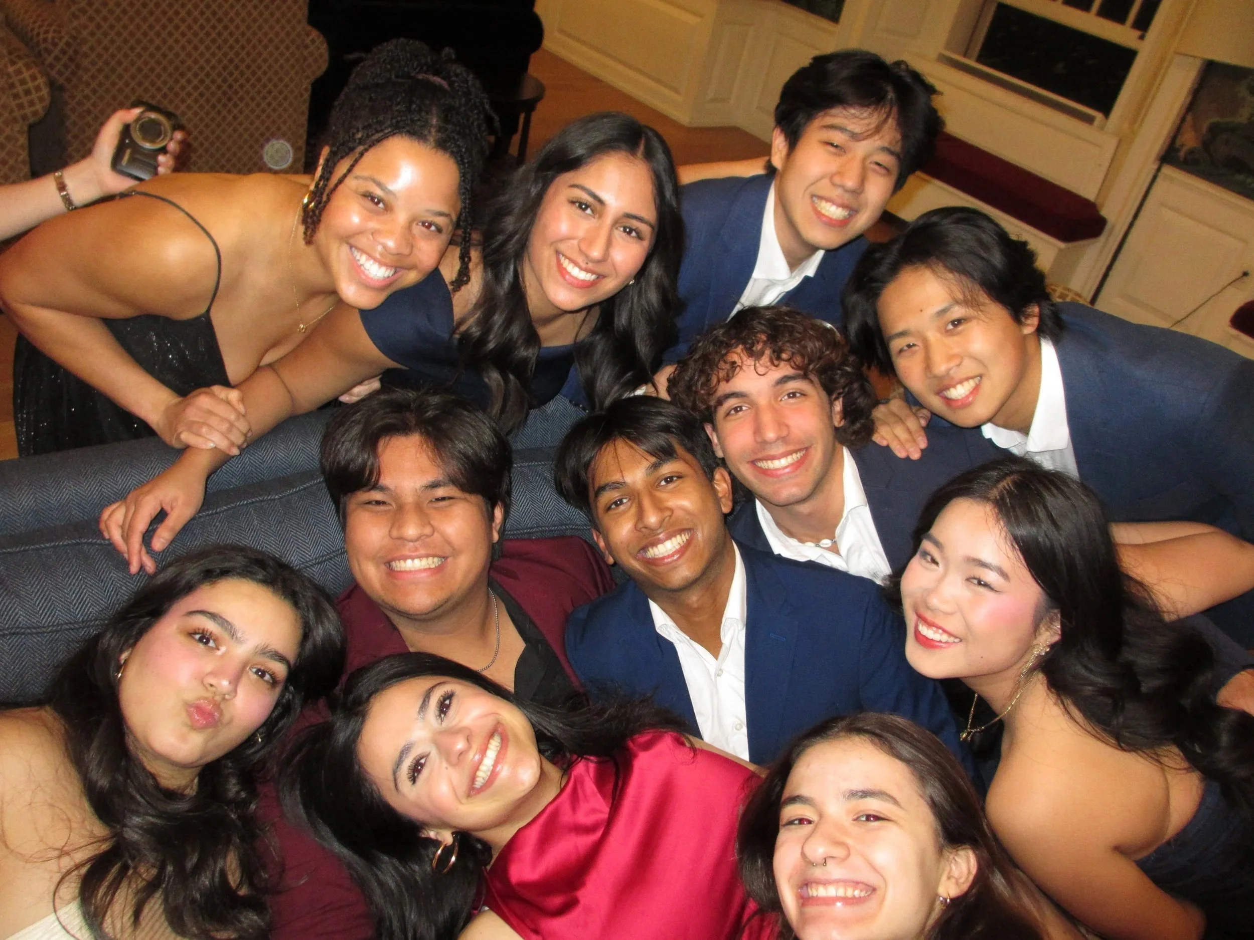Group of young adults smiling and taking a selfie at a social gathering in an indoor setting.
