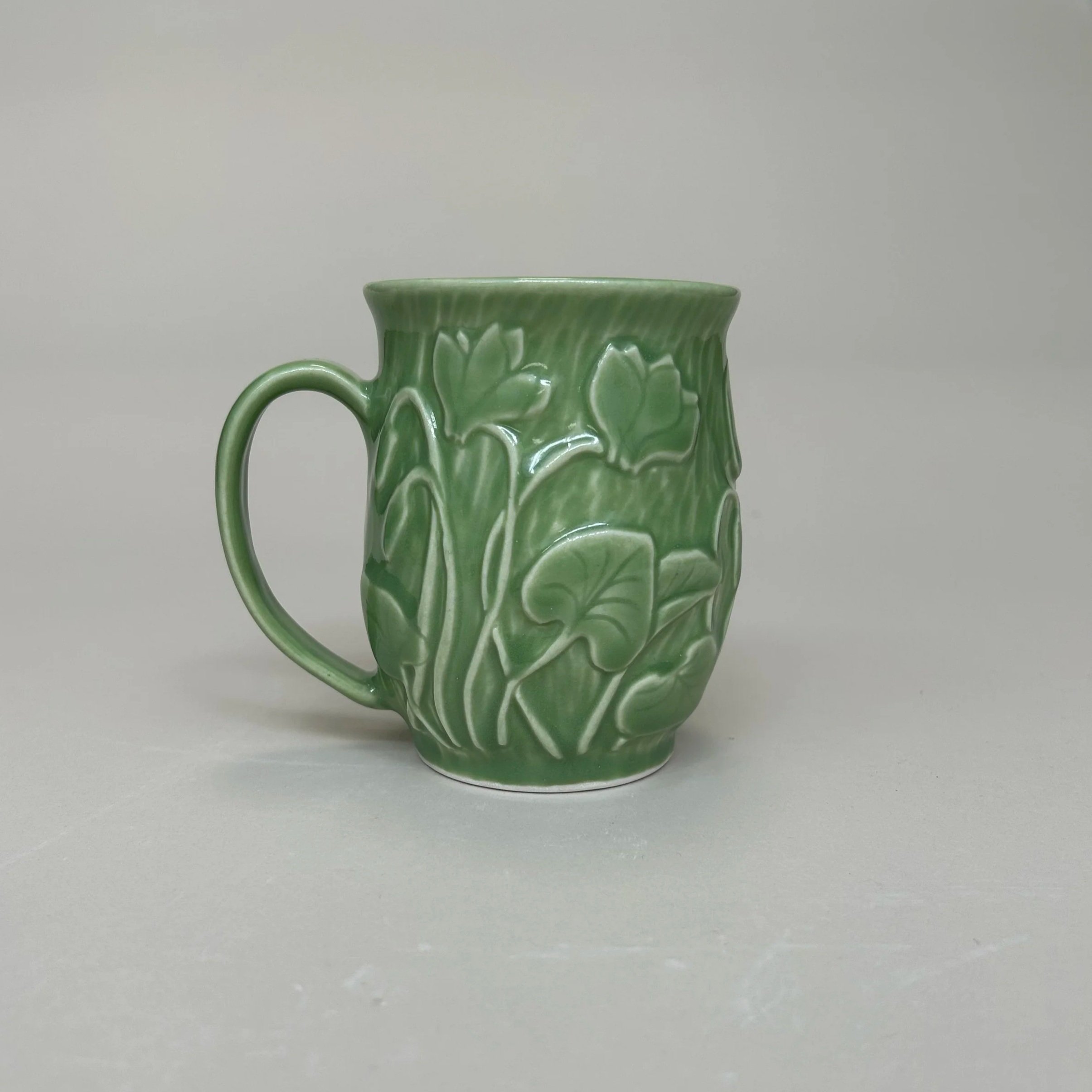 Green ceramic mug with a floral design against a plain light background.