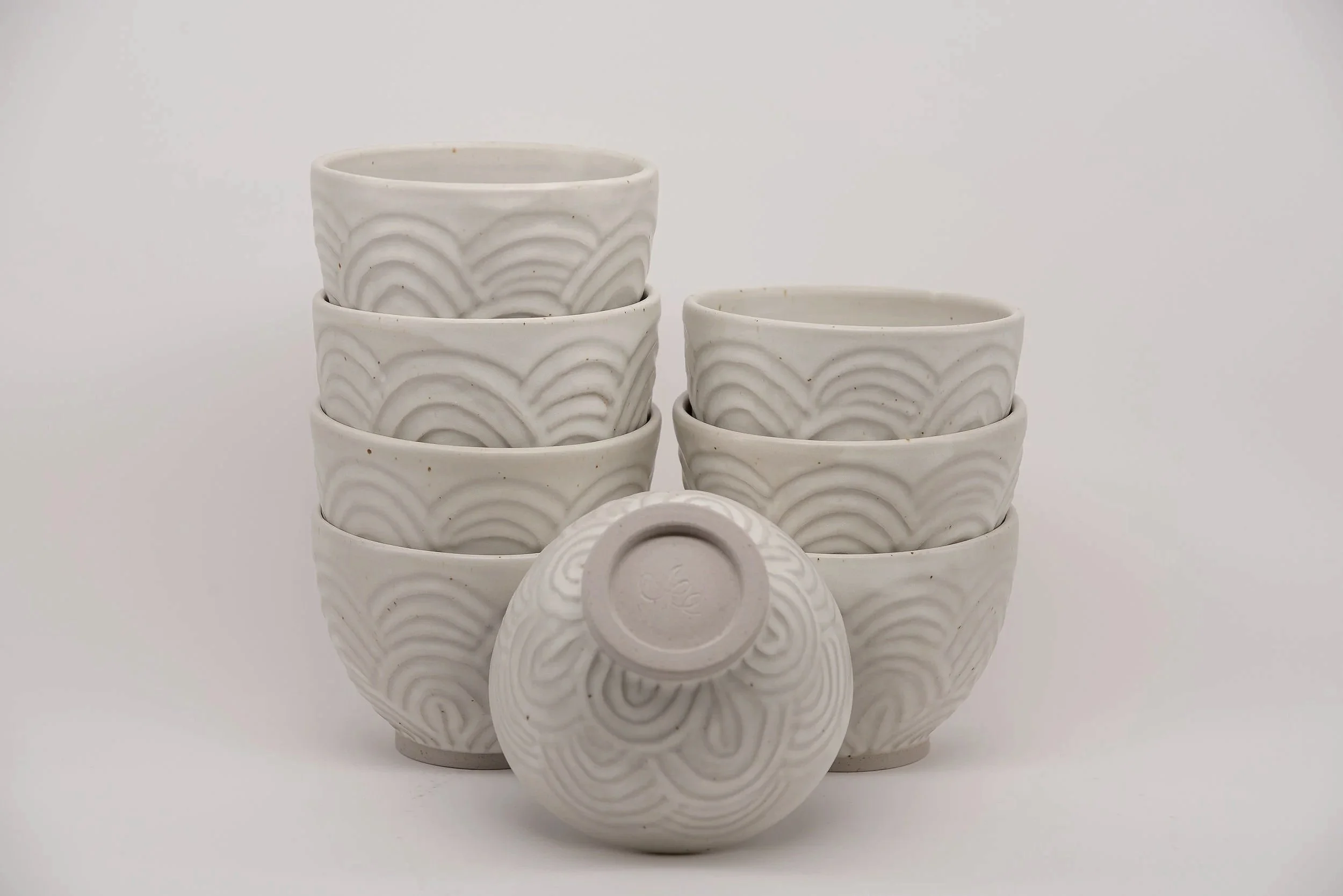Set of six white ceramic bowls with wave-like pattern, stacked in two columns, with one cup upside down in front.