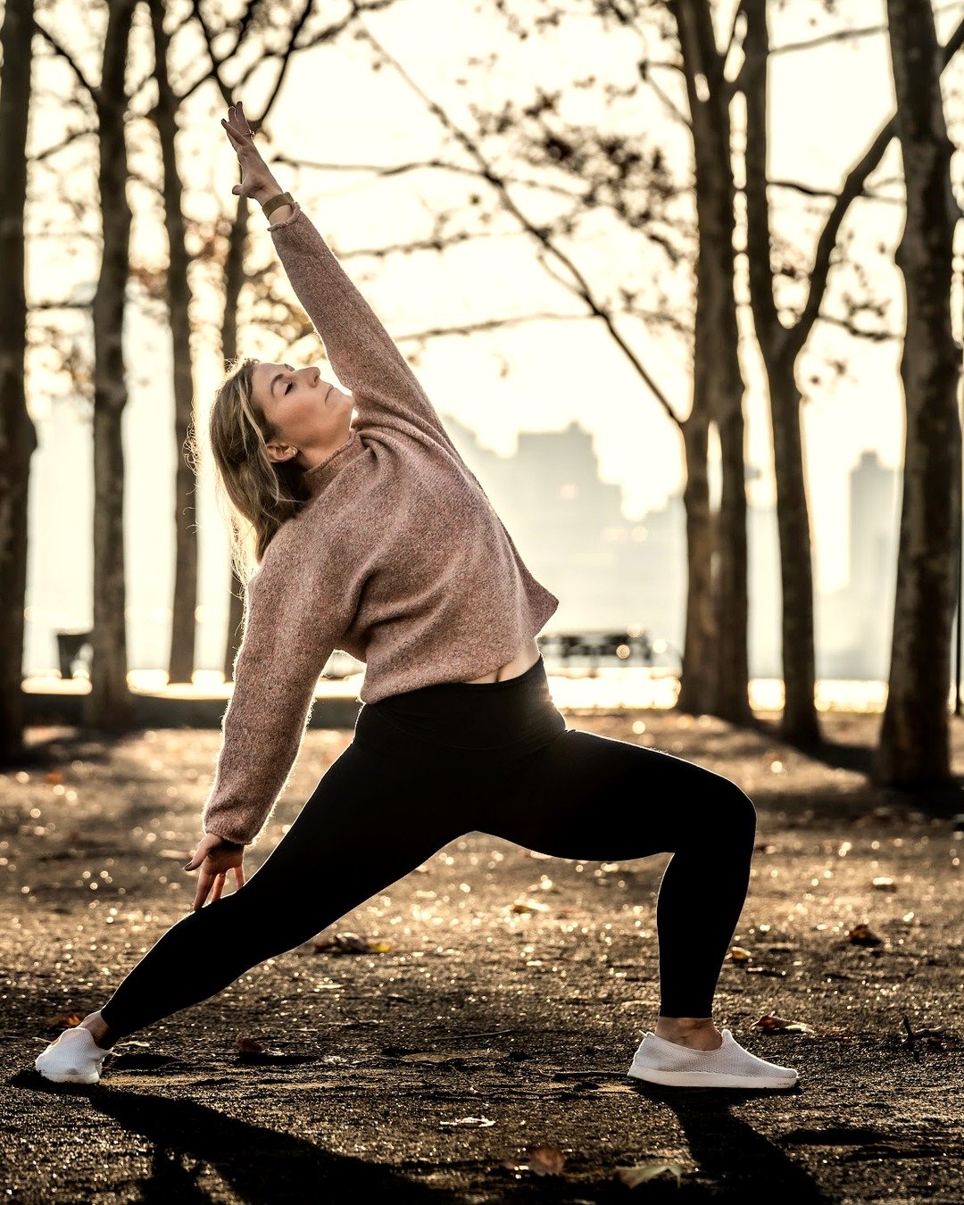 Teacher Danielle Tideman in Viparita Virabhadrasana among autumn trees, warm golden backlight