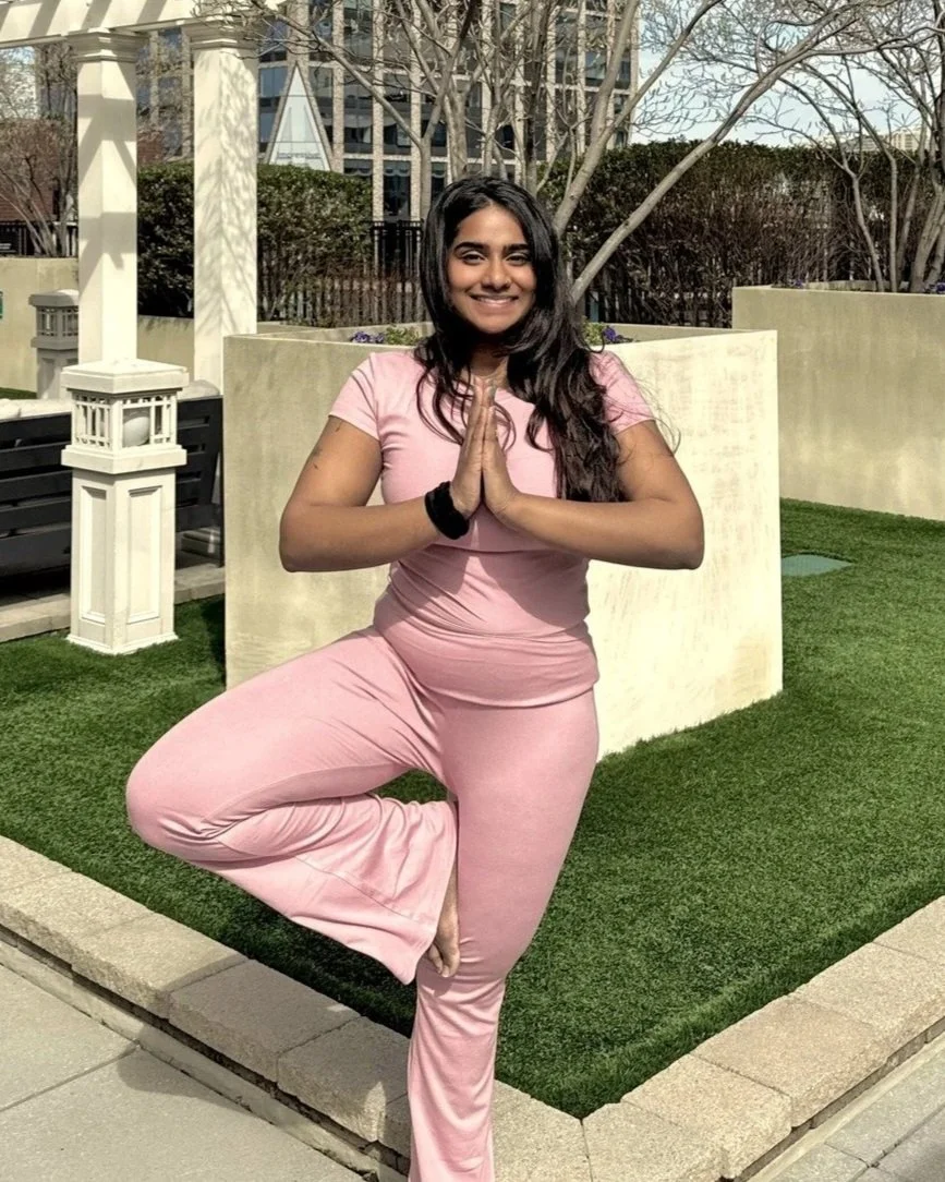 Nandita Shyam in Vṛkṣāsana (tree pose) with hands in prayer, smiling outdoors