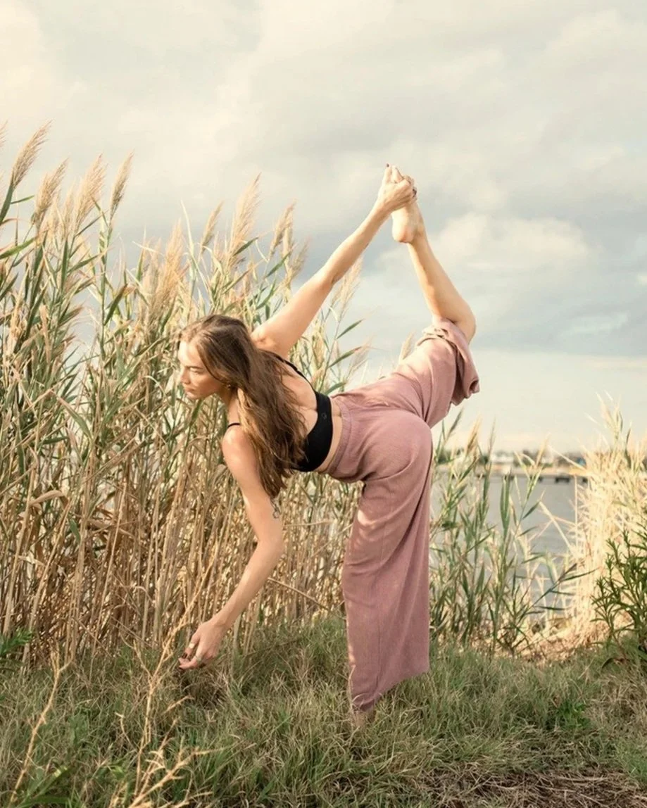 Claire Bilavsky in a dancer pose, Naṭarājasana, among tall golden grasses