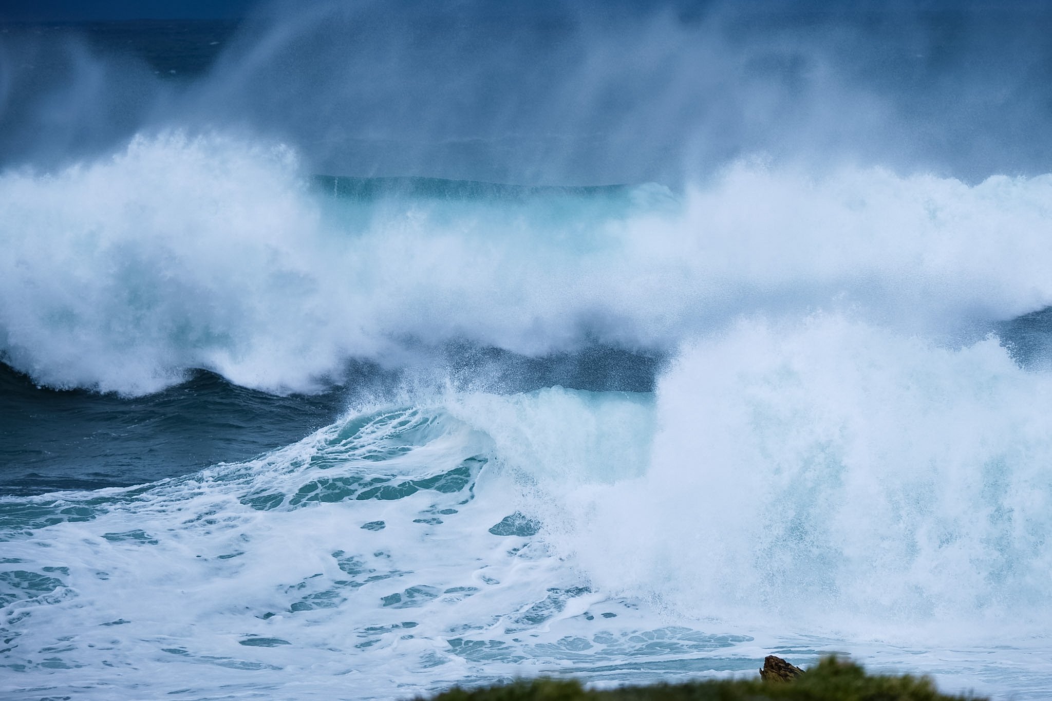 Large ocean wave crashing against rocks along the shoreline during daytime