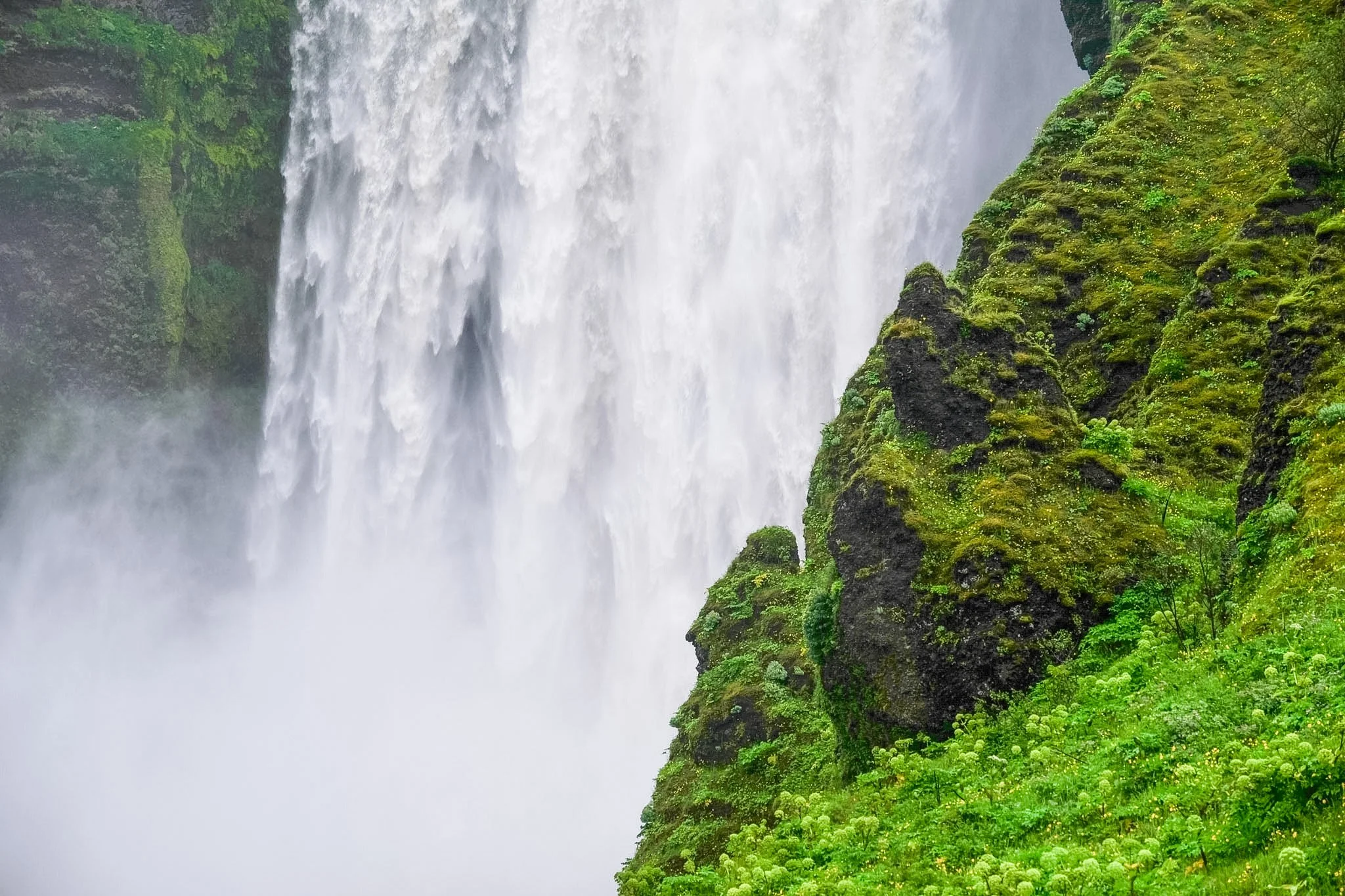 A large waterfall surrounded by lush green moss and trees in a misty landscape.