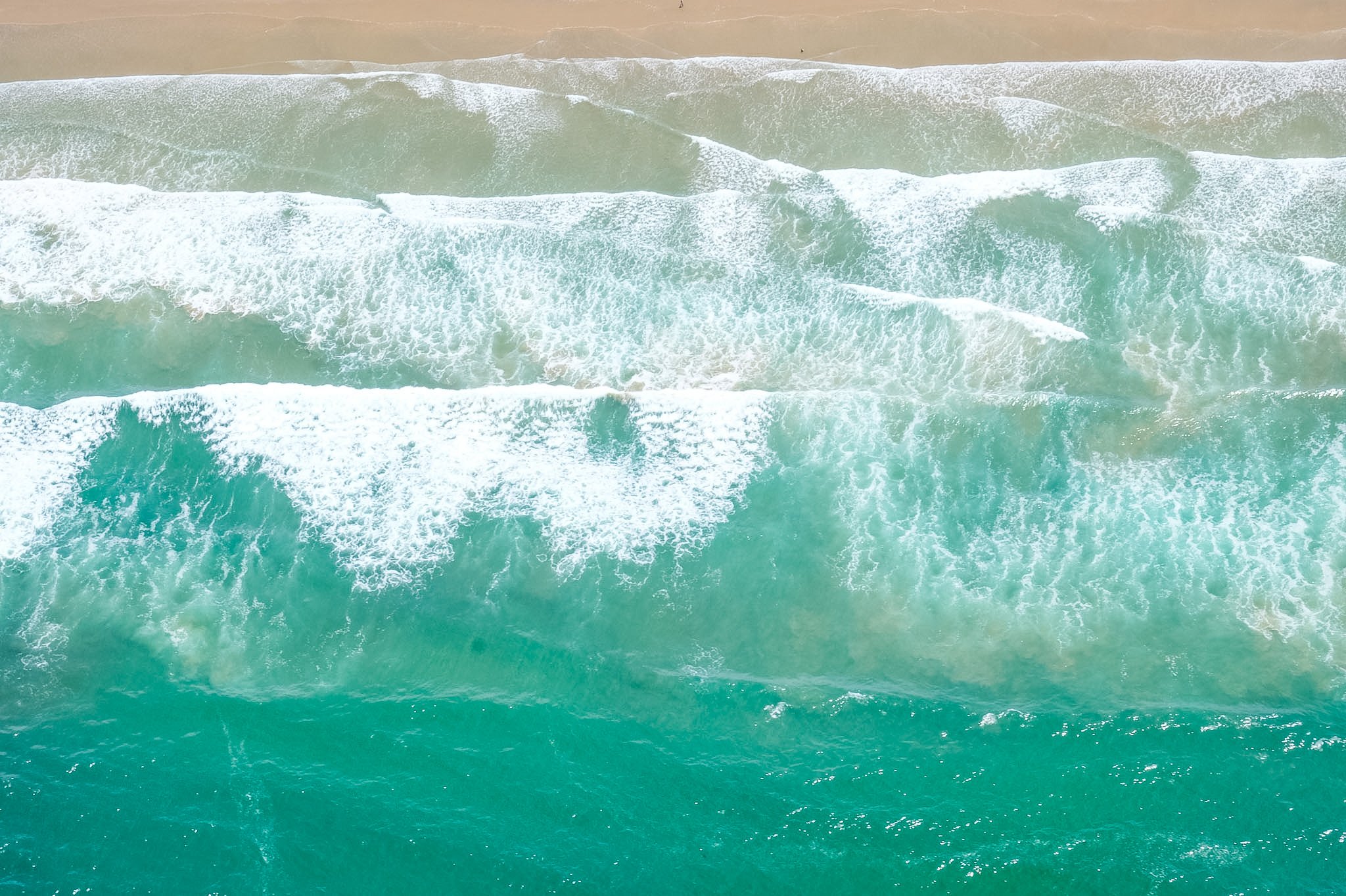 Aerial view of ocean waves crashing onto a sandy beach.