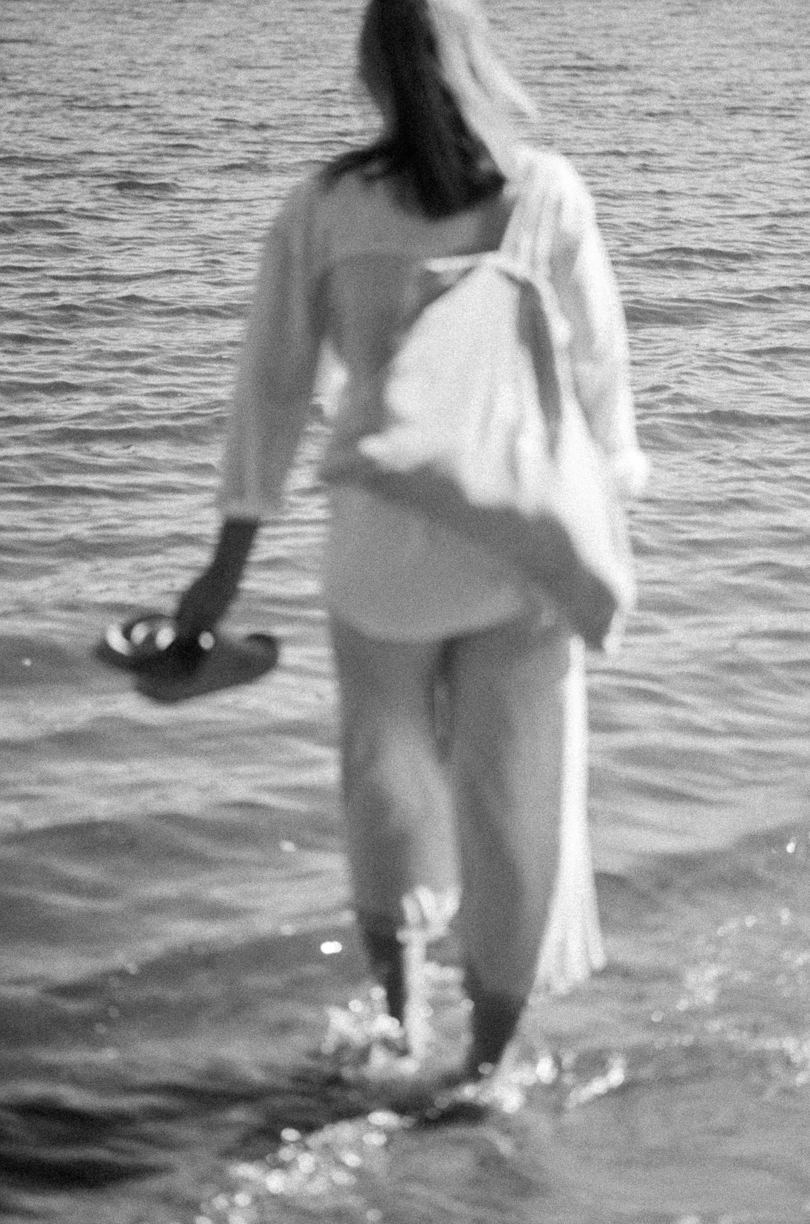 A person holding a fish on a beach near the water, with a towel wrapped around their shoulders.