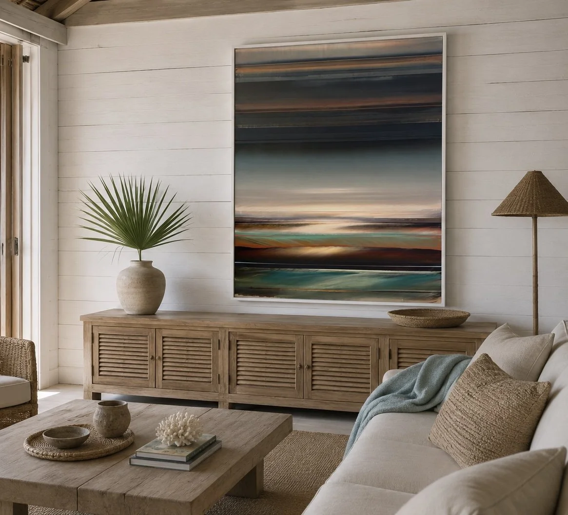 Living room with beige sofa, decorative pillows, wooden coffee table with books and coral sculpture, wooden sideboard with large potted palm, abstract landscape artwork, floor lamp, and natural decor in a coastal style.