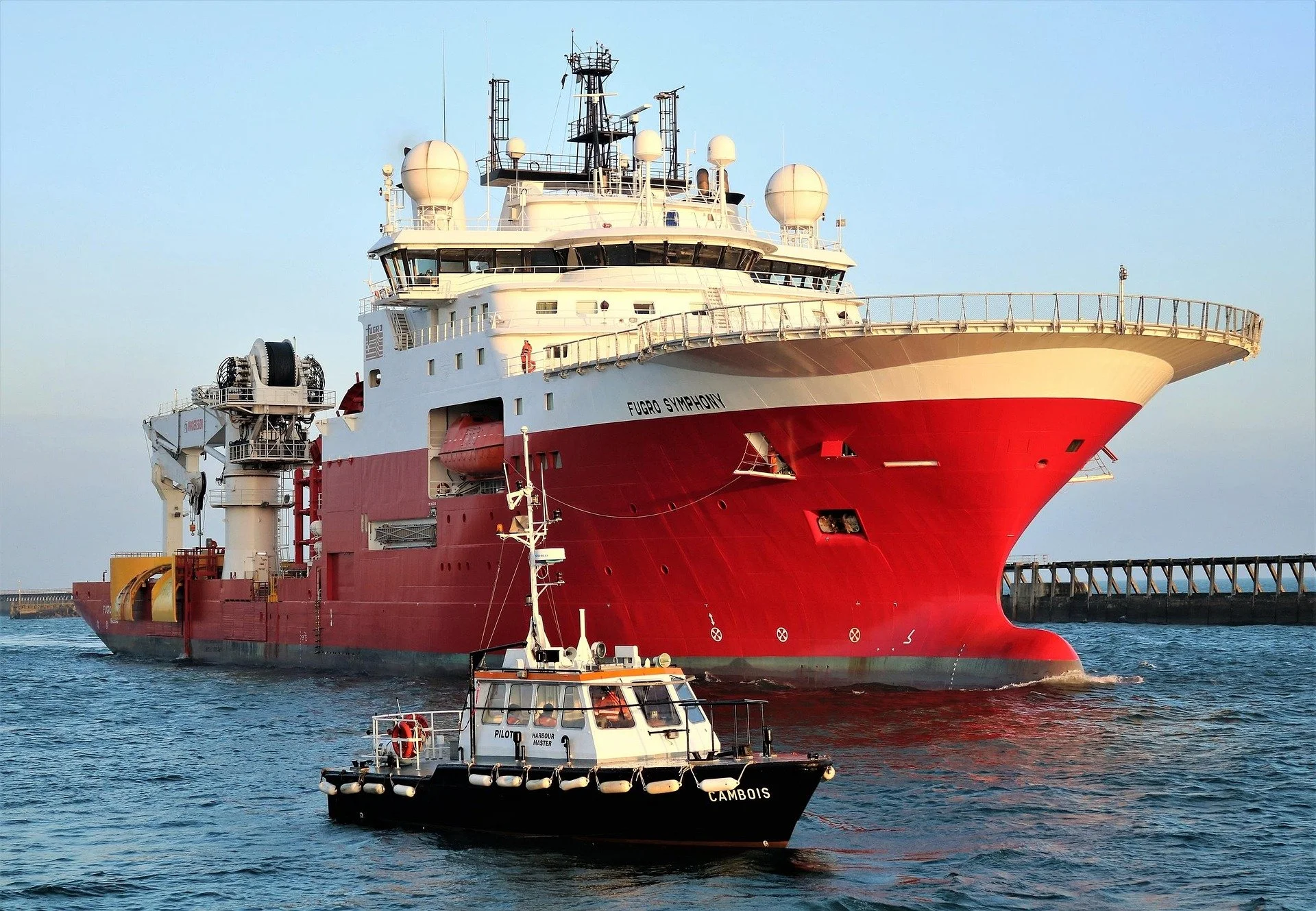 Large red and white cargo vessel Fugro Symphony docked at port, symbolizing international shipping and customs.